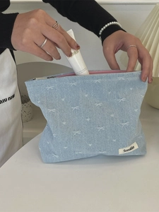 Denim makeup bag with white bow embroidery and zip closure shown in use with skincare