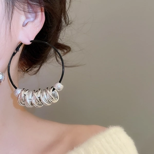 Close-up of black leather hoop earring with silver rings and white pearls on a model