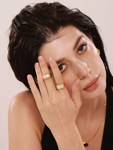 Dettaglio di anelli placcati oro con intarsio in madreperla bianca indossati da modella