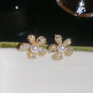 Makroaufnahme eines goldene Blumenohrsteckers mit weißer Perle und funkelnden Zirkonia