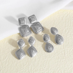 Juego de cuatro pendientes geométricos plateados con formas cuadradas y de gota sobre seda