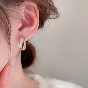Close-up of gold double-layer C-shaped earrings with mother of pearl and zircon stones