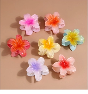 Flat lay of colorful resin plumeria flower hair claws in seven gradient shades