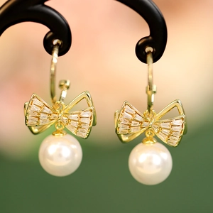 Macro view of gold bow earrings with square zircons and glossy white pearls