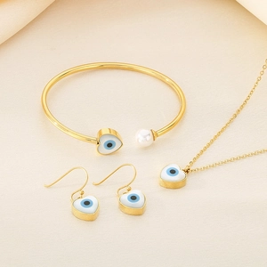 Detail view of gold jewelry set with evil eye heart charms and pearls on soft fabric