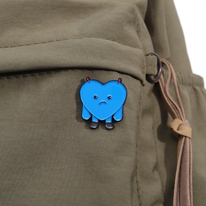 Detail of blue heart enamel pin with angry expression on an olive nylon backpack