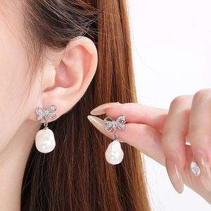 Close-up of silver bow earrings with sparkling stones and white baroque pearl drops