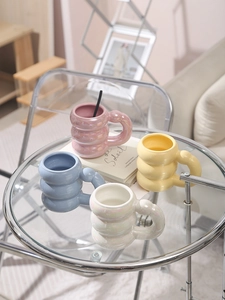 Close-up of four aesthetic bubble-shaped ceramic mugs in pastel colors on a glass table