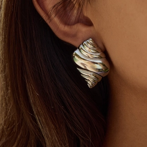 Macro side view of silver spiral shell-shaped earrings with metallic luster on model