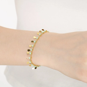 Detailed view of light green beaded bracelet with golden teardrop charms on a model wrist