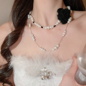 Detail of double-layer pearl necklace featuring a large black fabric flower and silver chain