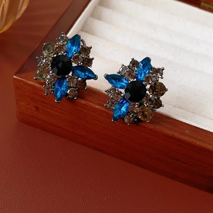 Dettaglio di orecchini vintage a fiore con cristalli blu e neri su superficie in pelle