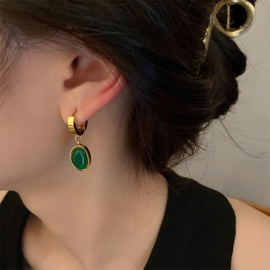 Detail of model wearing emerald green oval pendant earrings with golden titanium steel