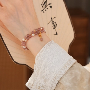 Close-up of double-layer strawberry quartz and pearl bracelet with a golden bell charm