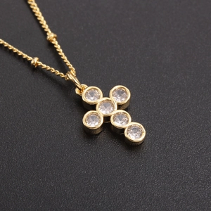 Golden cross necklace with six round clear zircons on a textured black background