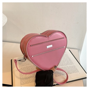 Detail of pink heart-shaped bag with silver zippers on leather texture surface