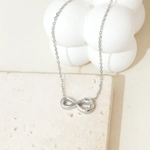 Detailed view of infinity heart necklace with zircon stone on beige stone pedestal