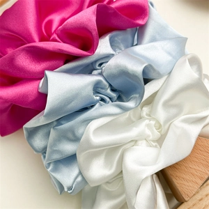 Glossy satin scrunchies in pink, blue, and white colors on a wooden stand
