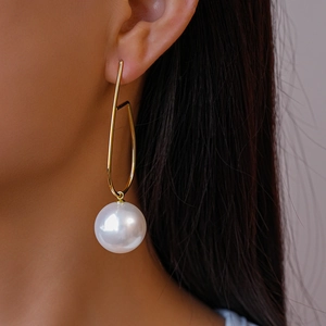 Dettaglio di modella che indossa orecchini a perla geometrici dorati dal design moderno