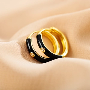 Detailed macro view of gold-plated hoop earrings with black enamel and zircons