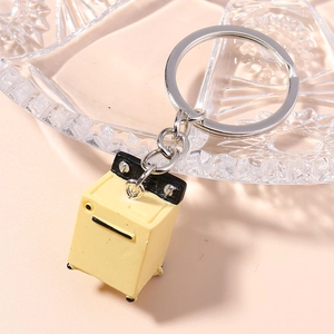 Miniature washing machine keychain with a light yellow finish on a glass tray background