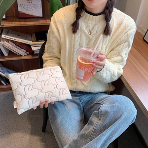Quilted white rabbit clutch bag with puffy bunny stitching in a cafe lifestyle setting