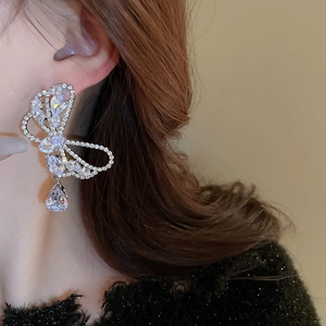 Close-up of a silver bow earring with a pear-shaped zircon drop on a female model