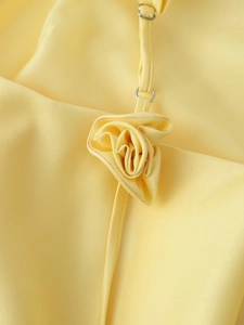 Detail view of a handcrafted yellow satin rose on the spaghetti strap of a summer dress