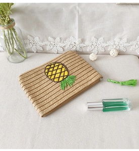 Close-up of straw woven clutch bag featuring pineapple embroidery and green tassel