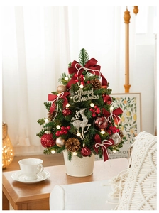 Close-up of a mini Christmas tree in a white bucket with red bows and warm LED lights