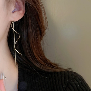 Macro shot of gold twisted wave earrings with delicate chain tassels on model