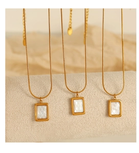 Détail macro de trois pendentifs dorés avec nacre blanche carrée et texture quadrillée