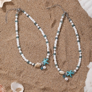 Detail of beach anklets with starfish, shell charms, and white beads on sand