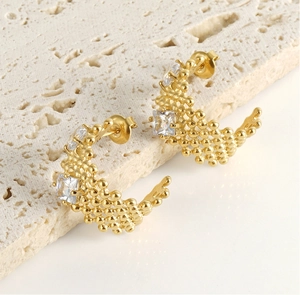 Détail de boucles d'oreilles C dorées avec texture perlée et trois zircons carrés sur pierre