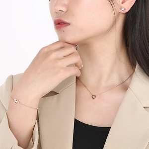Detail view of model wearing rose gold hollow heart necklace, bracelet and earrings set