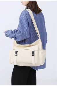 Vue latérale d'un modèle portant un sac messager en toile beige avec boucles et poche