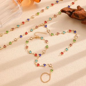 Artistic close-up of gold body chain with multi-colored heart gems on sandy background