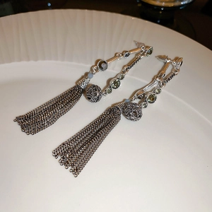 Detailed macro view of silver tassel drop earrings with colorful inlaid crystals on white tray