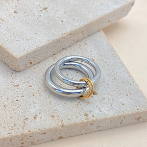 Detail showing interlocking silver rings with gold connectors on a textured stone base