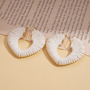 Detail of white yarn-wrapped heart earrings with gold bead trim on a vintage paper background