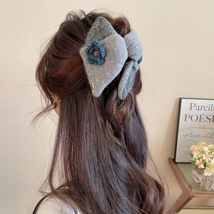 Detail of grey knitted bow hair claw with blue floral crochet on a half-up hairstyle