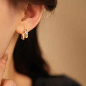 Détail de créoles dorées avec émail blanc et pierres de zircone étincelantes sur le lobe