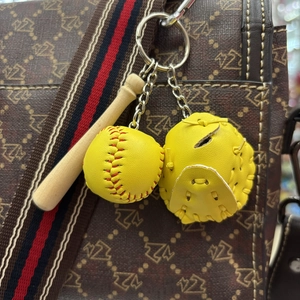 Detailed view of yellow baseball, glove, and wooden bat keychain on a designer bag