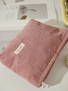 Pink corduroy makeup bag with H&R label on a minimalist desk for travel storage