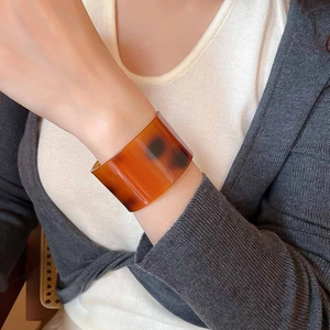 Macro detail of amber tortoiseshell wide cuff bracelet on wrist for a minimalist style