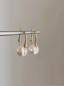 Close-up of elegant gold drop earrings featuring large white pearls on a minimalist stand