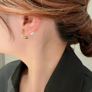 Detailed close-up of a model wearing minimalist gold C-shaped earrings with faux pearl detail