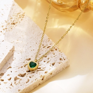 Detail shot of a gold heart necklace with a green gemstone on a travertine stone