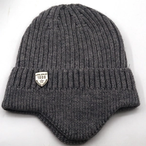 Close-up of deep grey rib-knit beanie showing the silver metal shield logo and texture