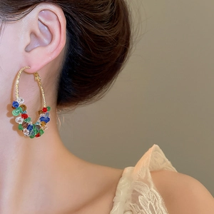 Close-up of golden hoop earrings featuring colorful beads on a model's ear